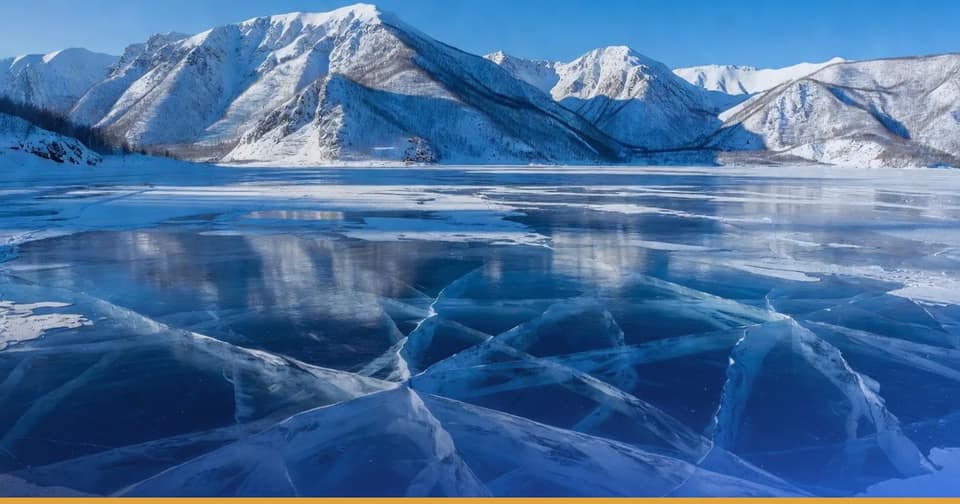 La glace bleue et fendue du lac Baïkal en hiver, au pied de montagnes enneigées