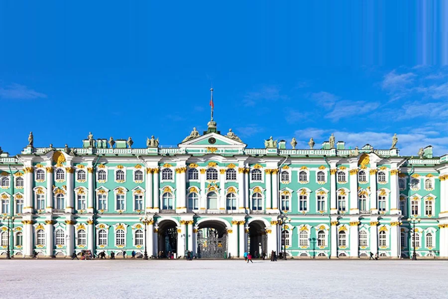 La façade vert et blanc du palais d'Hiver sous un ciel bleu, la place du Palais couverte de neige